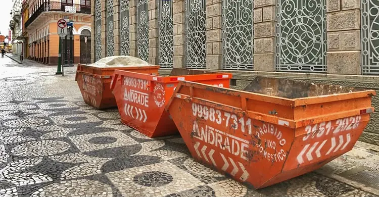 Três caçambas laranja da Andrade em uma rua de petit-pavé no centro histórico de Curitiba