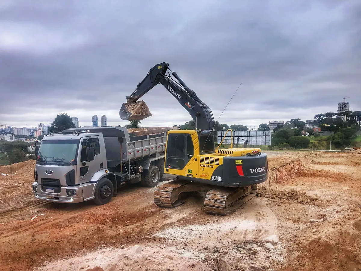 Caminhão basculante da Andrade sendo carregado com terra por uma escavadeira Volvo