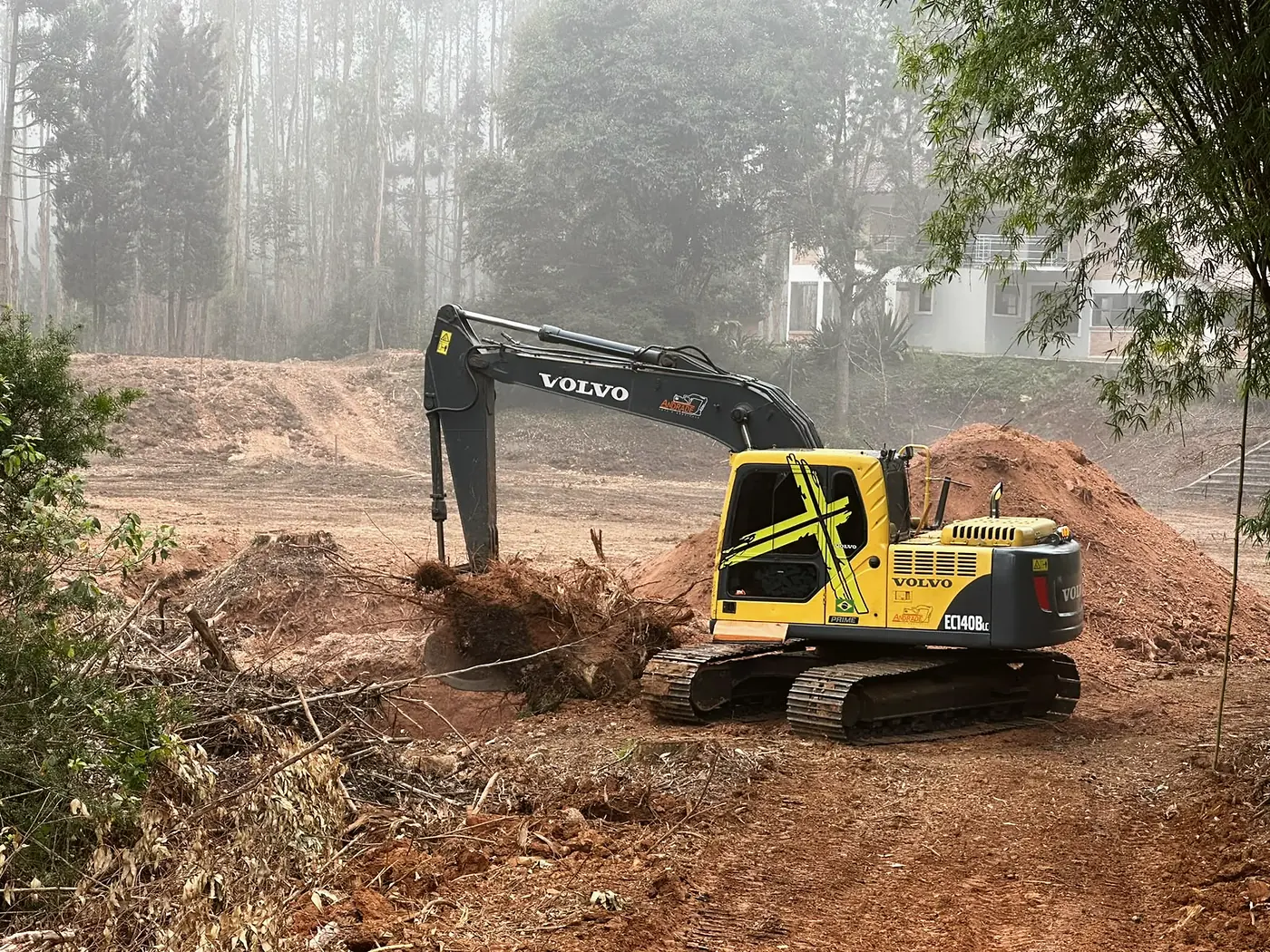 Escavadeira Volvo retirando vegetação e tocos de um terreno